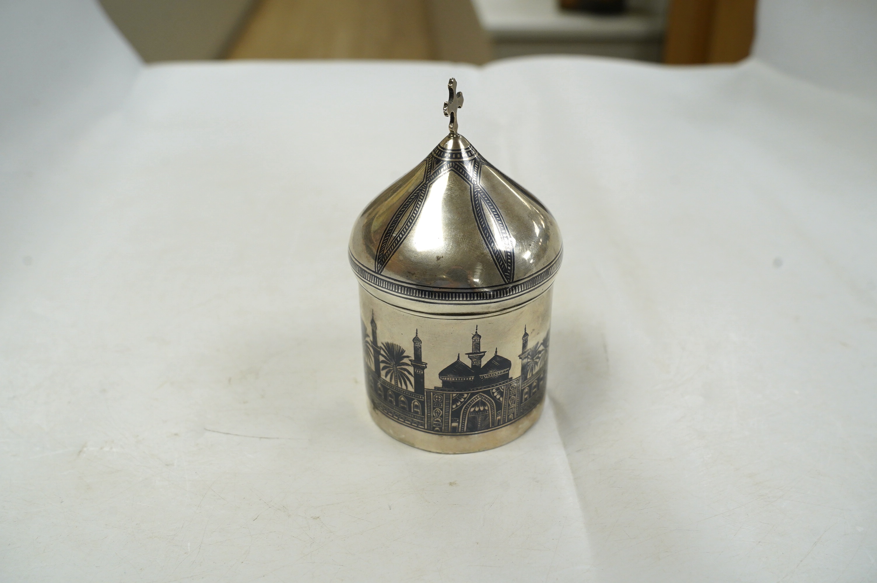 A Middle Eastern white metal and niello box and cover, with cross finial, 11.8cm, gross weight 4.4oz. Condition - poor to fair